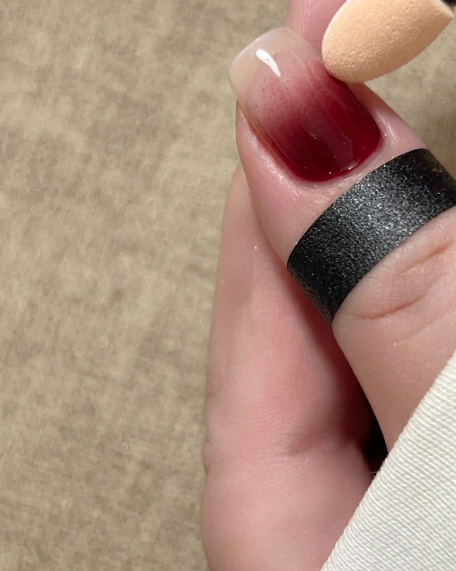 Un applicatore in spugna che sfumina dolcemente il pigmento rosso con un gradiente ombré lungo ununghia.