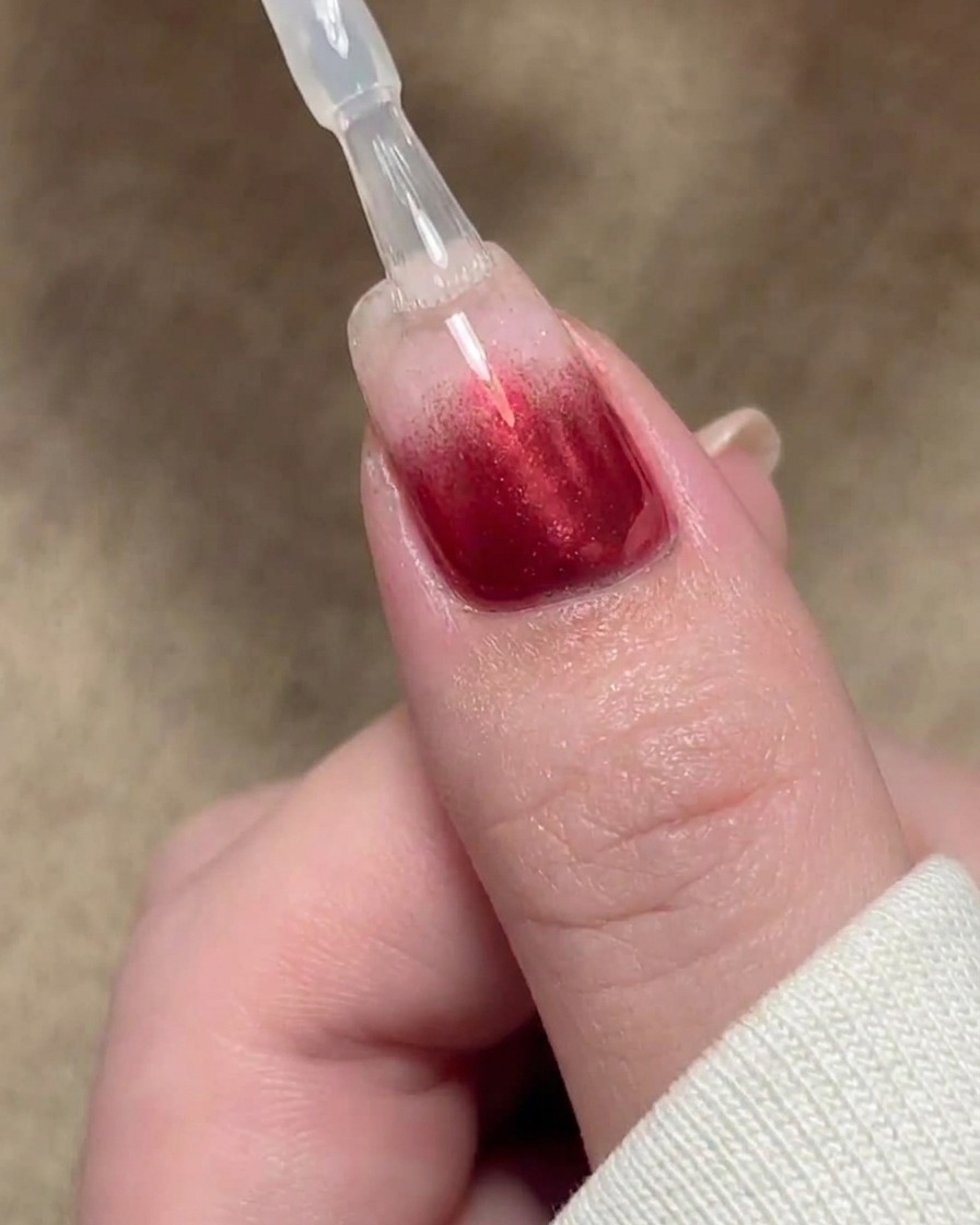 Un pennello che applica uno strato sigillante trasparente di base gel su un design per unghie con sfumatura rossa.