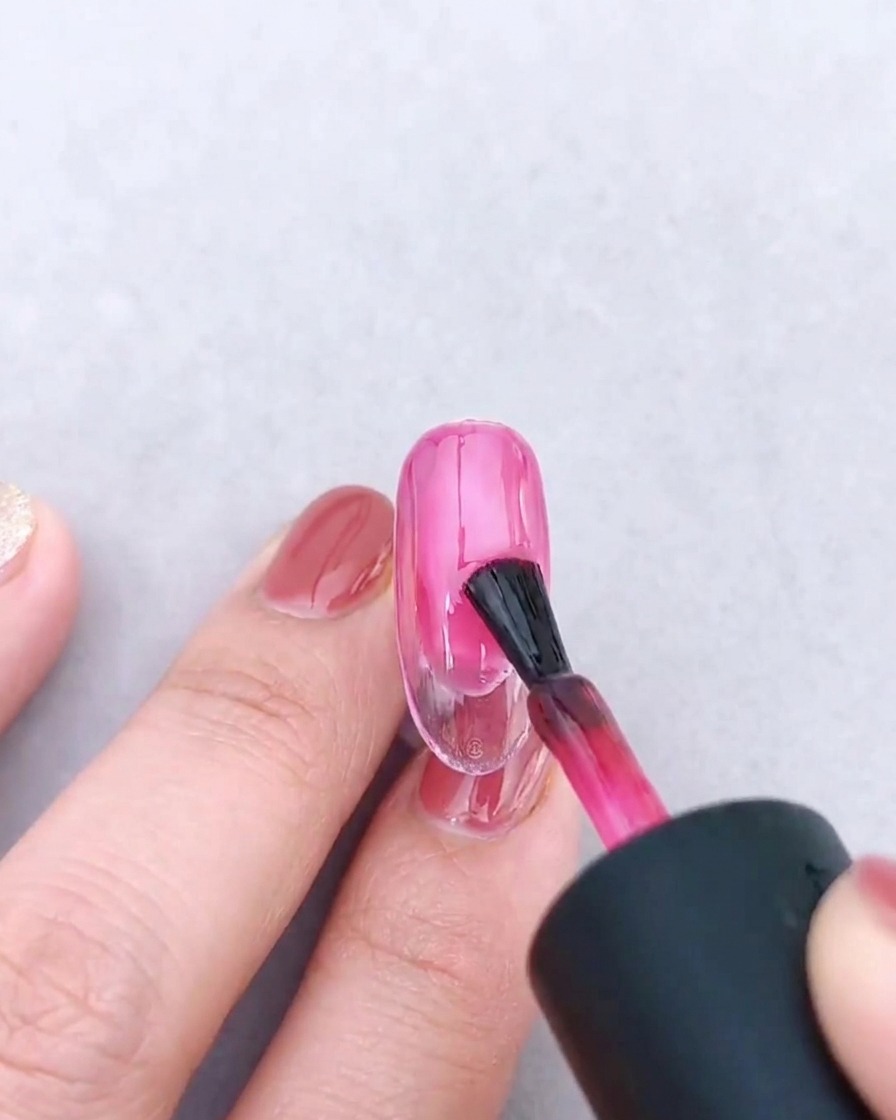 Un pennello per unghie che applica una seconda mano di gel rosa traslucido sulla sfumatura esistente.