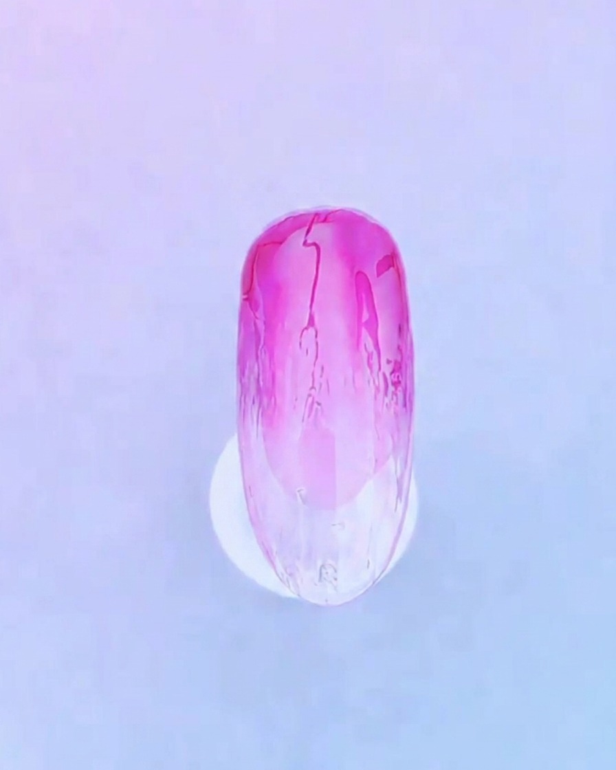 Primo piano di un pennello per unghie che applica uno strato trasparente e uniforme di gel di base sul design esistente delle unghie sfumate rosa.