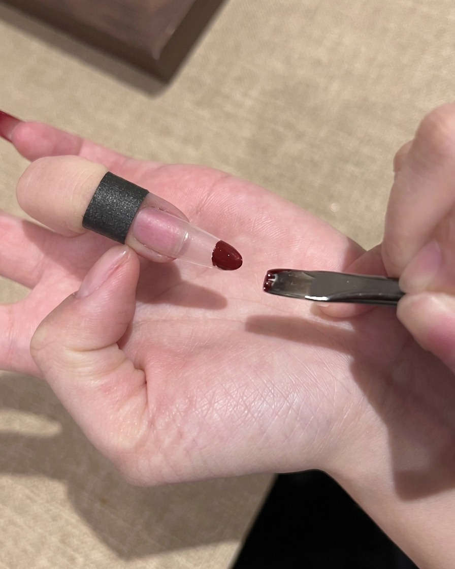Una mano che utilizza una piccola spugnetta per tamponare lo smalto gel rosso sulla punta di unestensione per unghie trasparente.