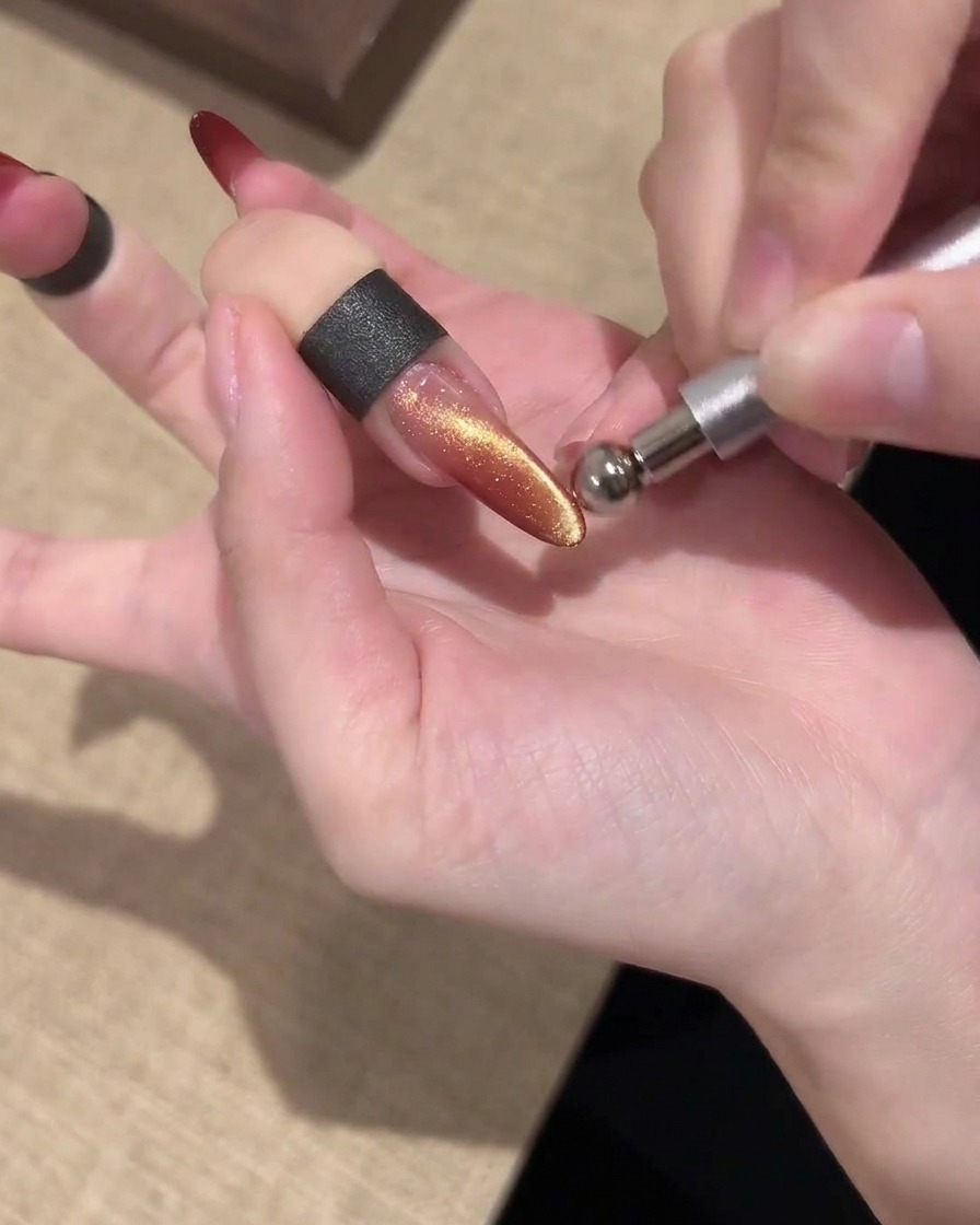 Un magnete a barra tenuto parallelamente sopra ununghia cat eye dorata e rossa brillante per modellare la luce.