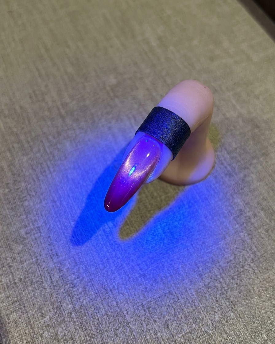Ununghia sotto una lampada UV blu che mostra una finitura cat eye lucida.