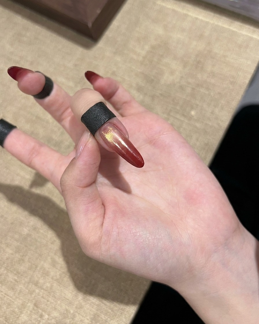 Ununghia cat eye sfumata rossa finita con accenti dorati mostrata su una mano.