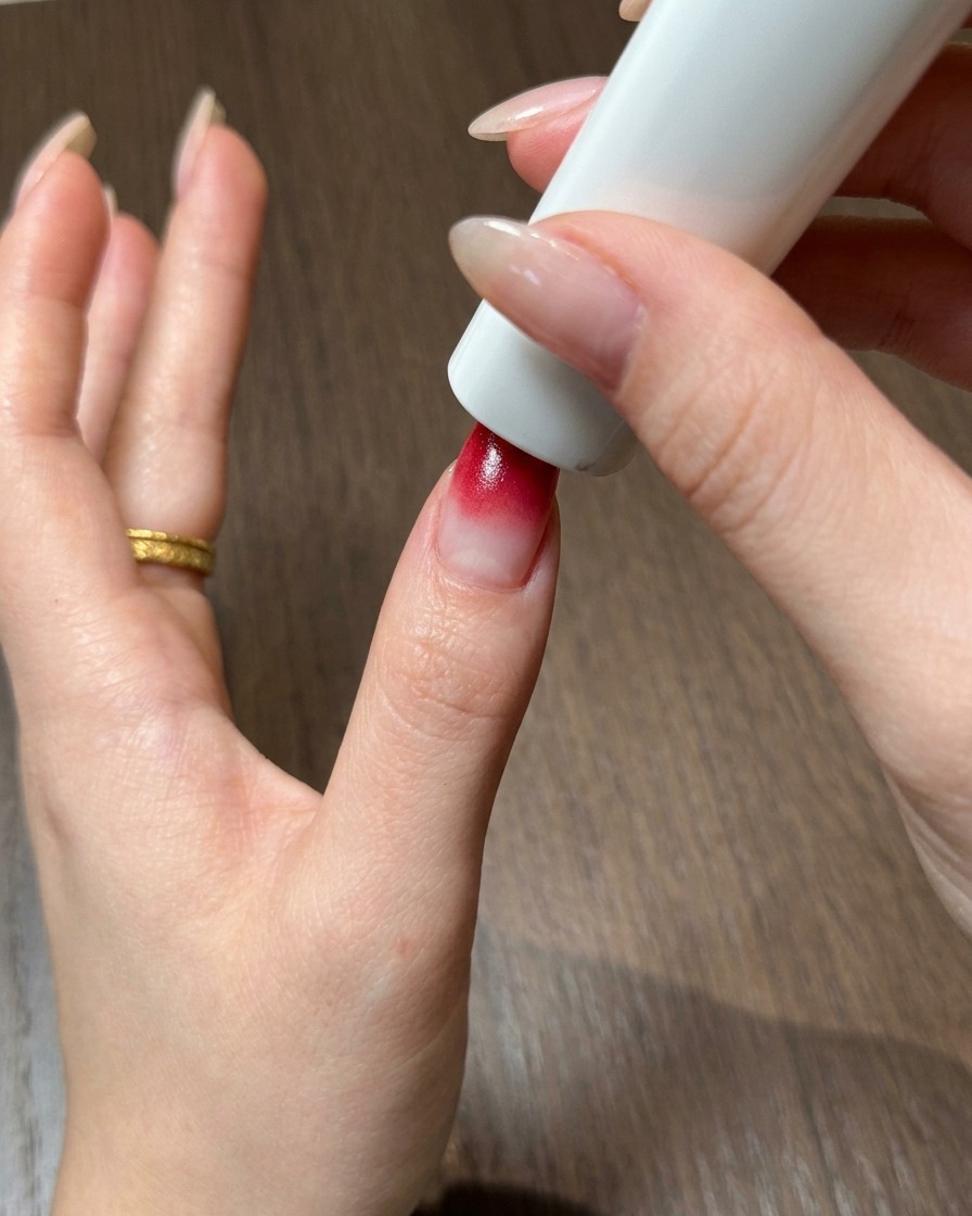 Un pollice posizionato direttamente sotto una lampada per unghie UV e LED portatile per polimerizzare il gel ombré rosso.