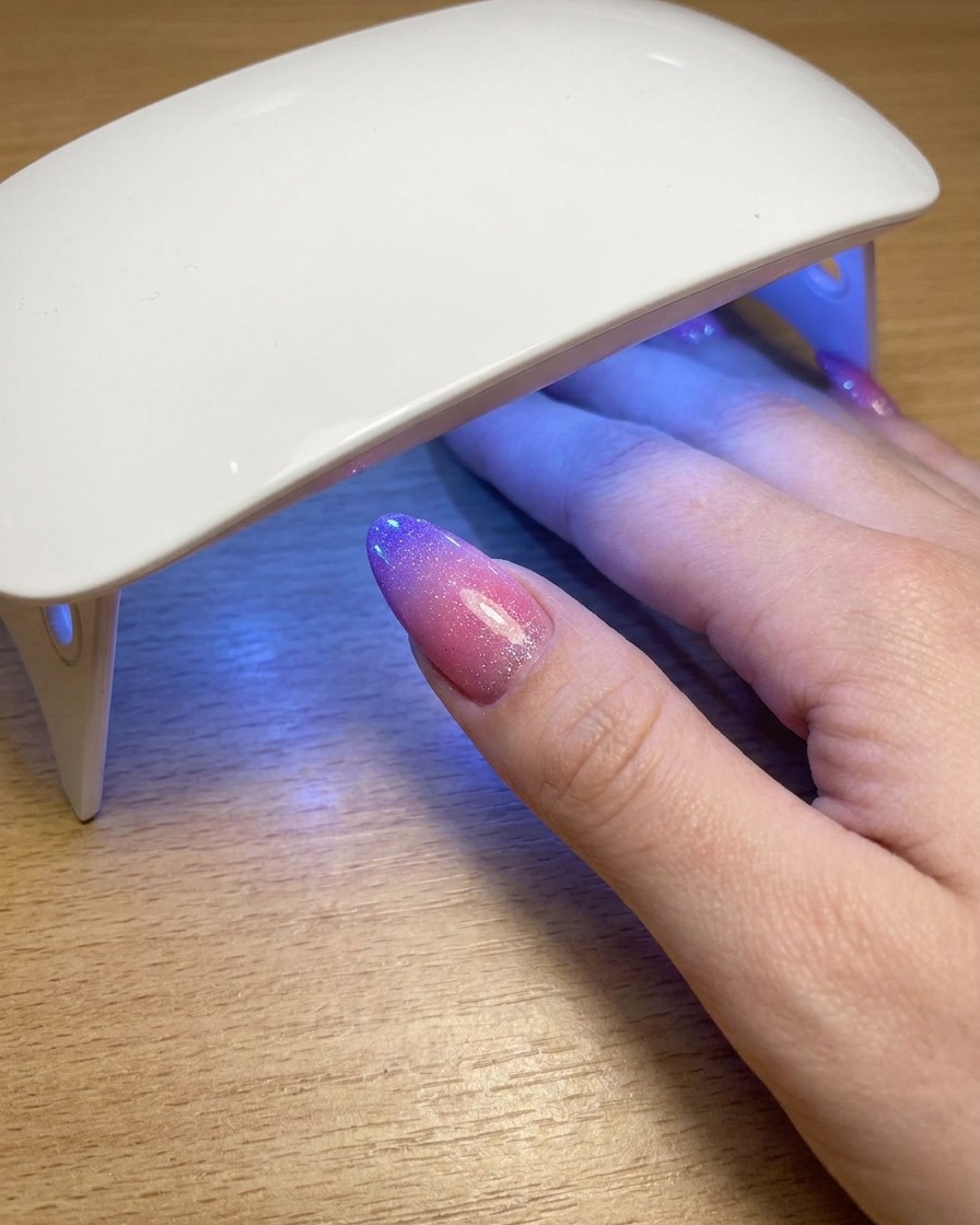 Un pollice appoggiato sotto una lampada UV portatile mentre polimerizza lo strato finale di gel polish cat eye.