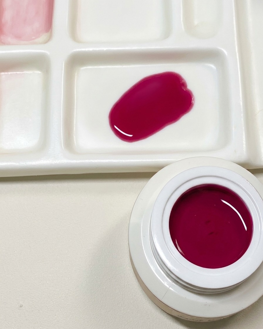 Tavolozza per la miscelazione con un campione di gel rosa scuro personalizzato accanto a un vasetto aperto di gel rosso pitaya.