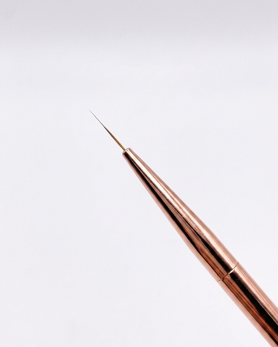 Vista in primo piano di un pennello liner oro rosa da 12 mm con punta affilata su uno sfondo neutro.