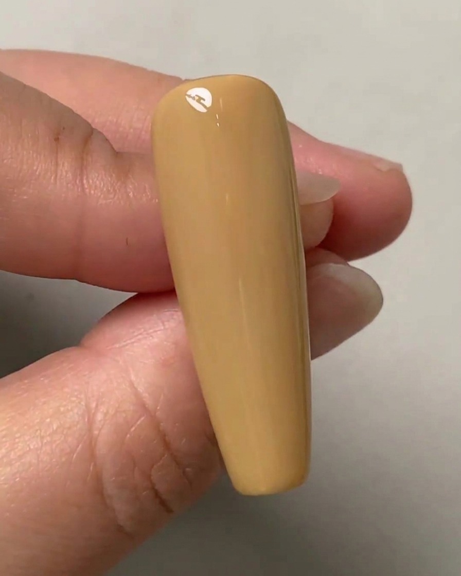 Una mano che regge ununghia di prova color nude con tre punti leggeri segnati verticalmente al centro.
