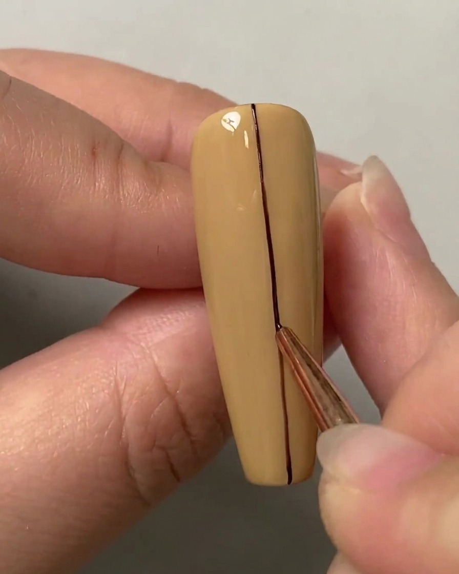 Un pennello liner che traccia una linea scura dritta lungo il centro verticale di ununghia color nude.