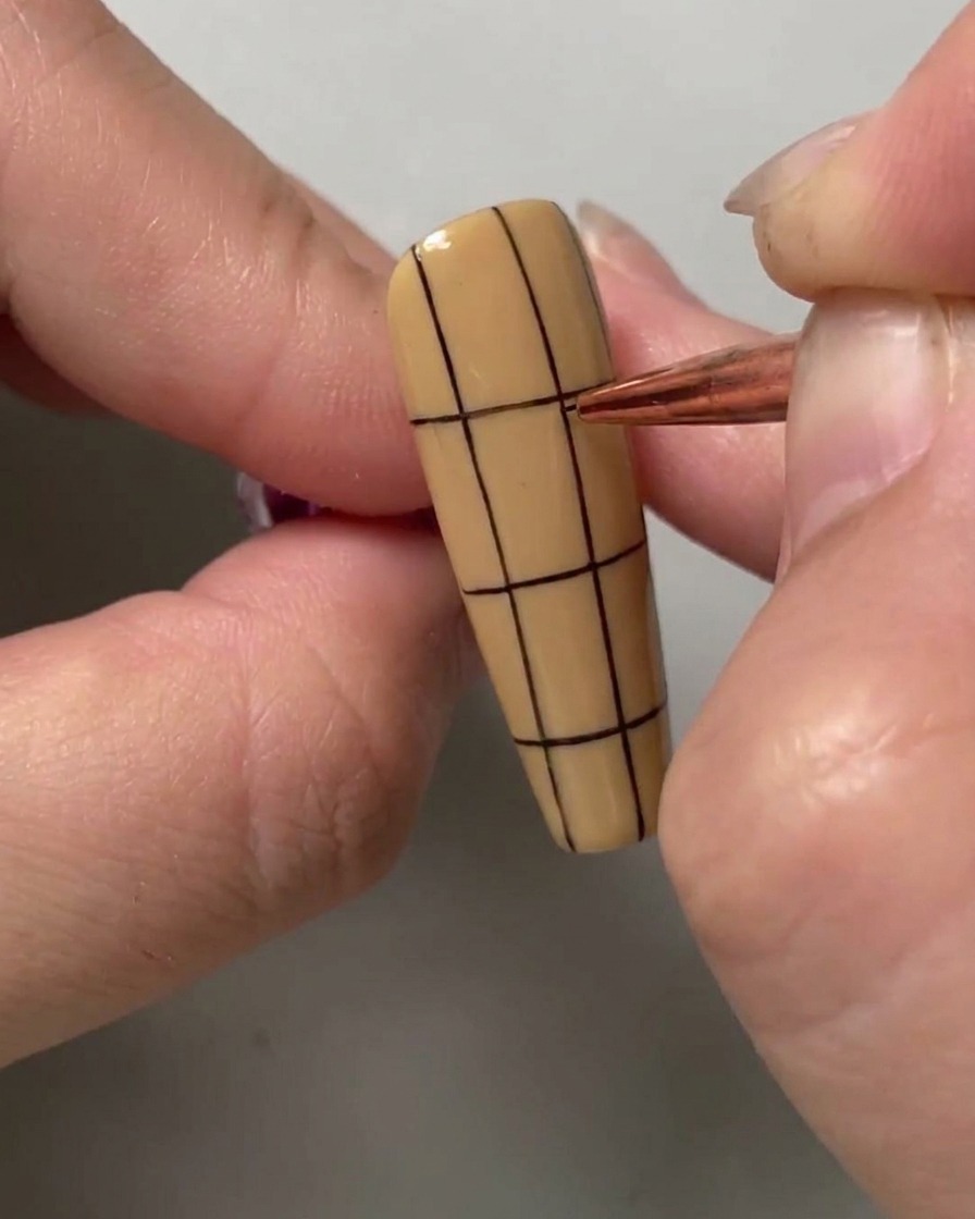 Un pennello per nail art che disegna una linea orizzontale nera nella metà superiore di ununghia a strisce verticali.