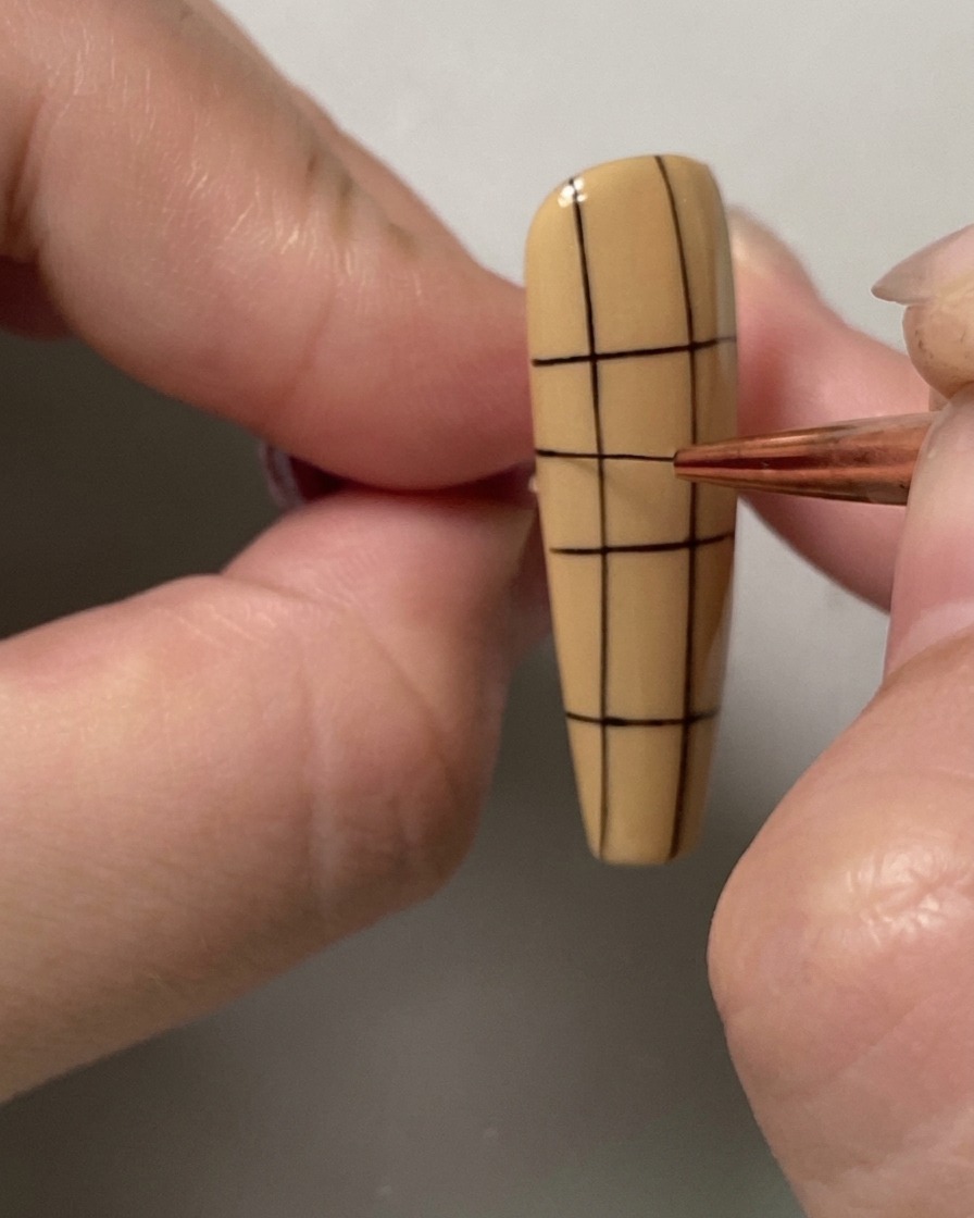 Un pennello liner sottile che aggiunge unulteriore linea orizzontale nella porzione superiore di una griglia su ununghia.