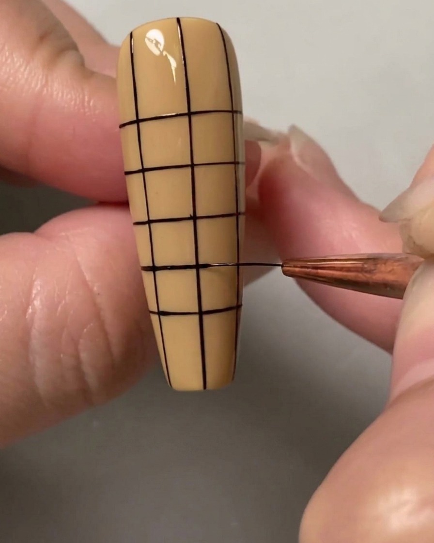 Un pennello per nail art che disegna le linee orizzontali finali per completare una griglia di piccoli quadrati regolari su tutta lunghia.
