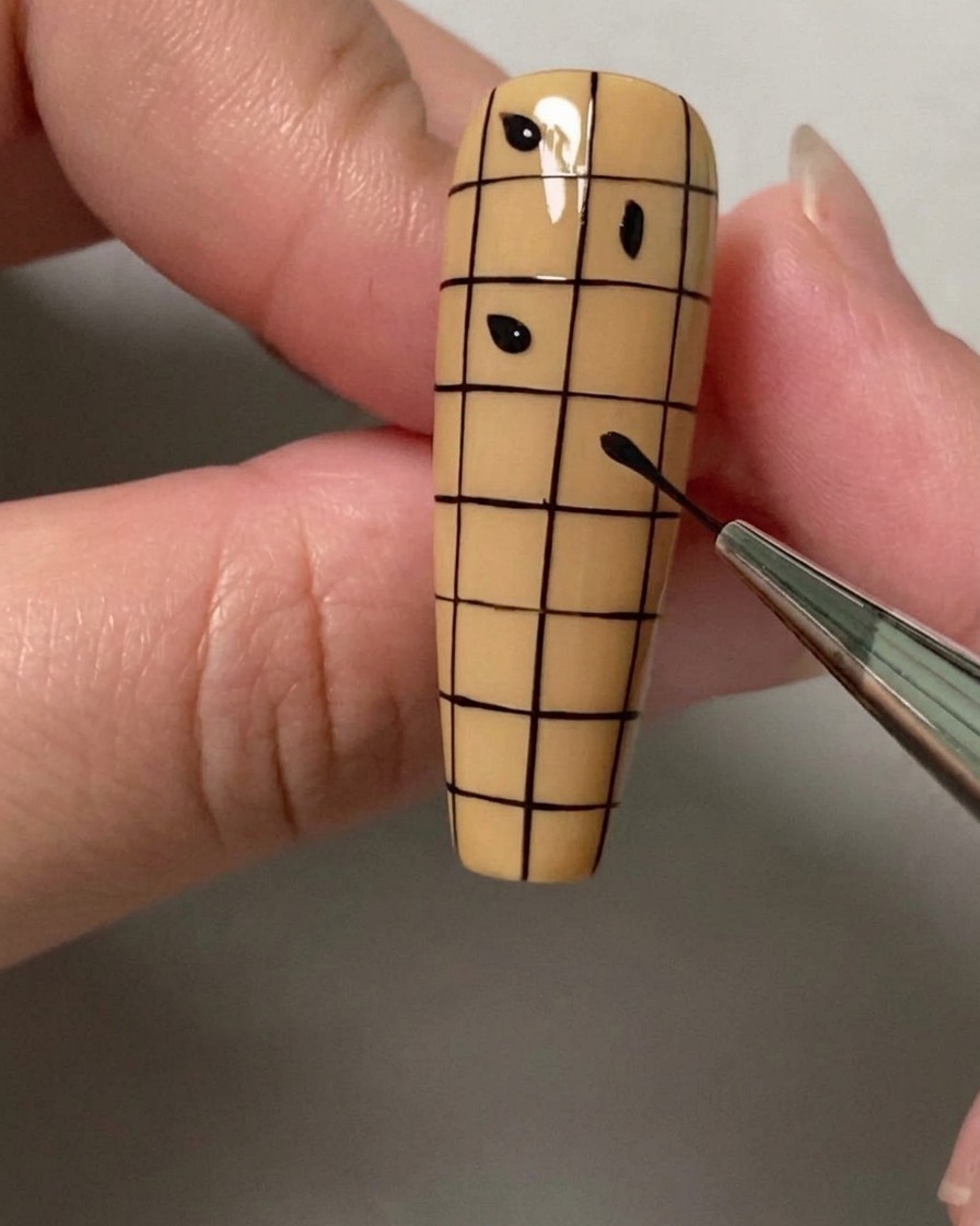 Un dotting tool o un pennello che posiziona piccoli punti neri nei quadrati alternati di una griglia su ununghia.