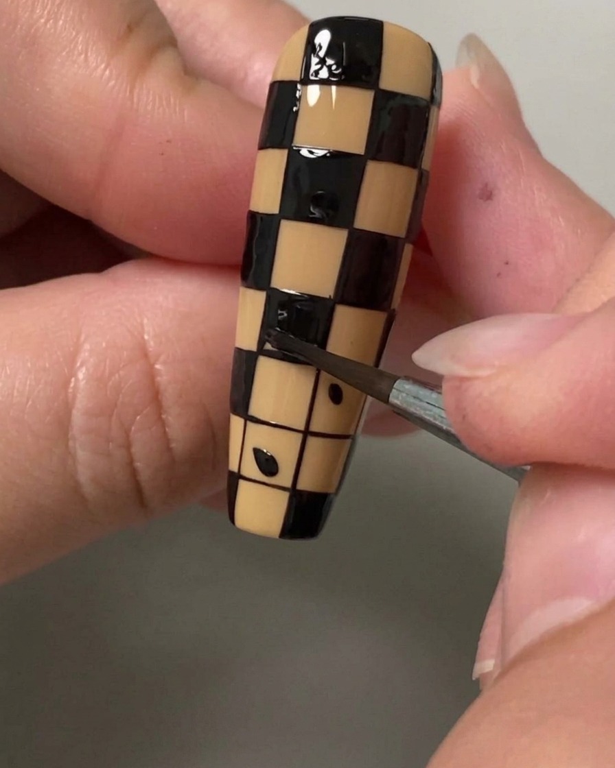 Primo piano di un pennello di dettaglio sottile che riempie un piccolo quadrato con smalto nero per creare un motivo a scacchi su ununghia.
