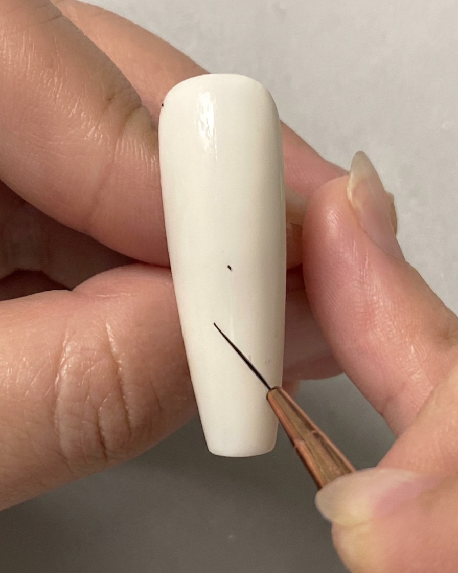 Una mano che utilizza un pennello liner sottile per posizionare un piccolo punto su ununghia bianca solida.
