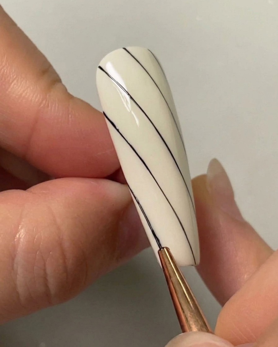 Un pennello per nail art che disegna una terza linea diagonale nera sul lato inferiore sinistro di ununghia dipinta di bianco.