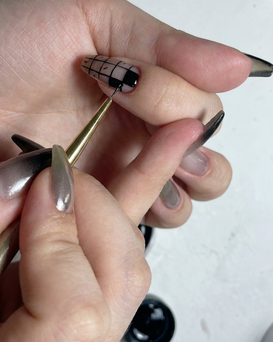 Un pennello fine che ritocca i bordi dei quadrati neri riempiti in un design di nail art a quadretti per renderli nitidi.