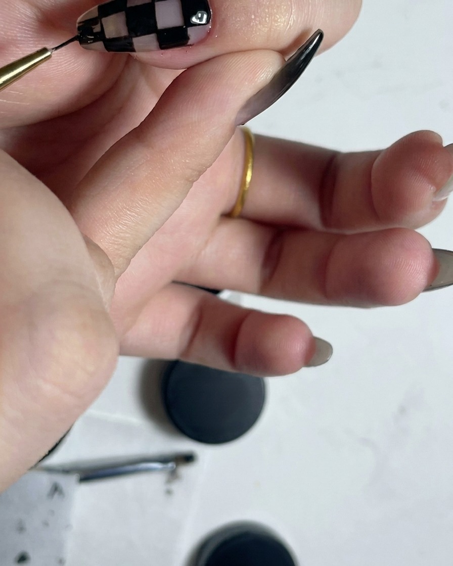 Un pennello liner sottile che delinea il perimetro di unghie completate con motivo a quadretti bianco e nero.