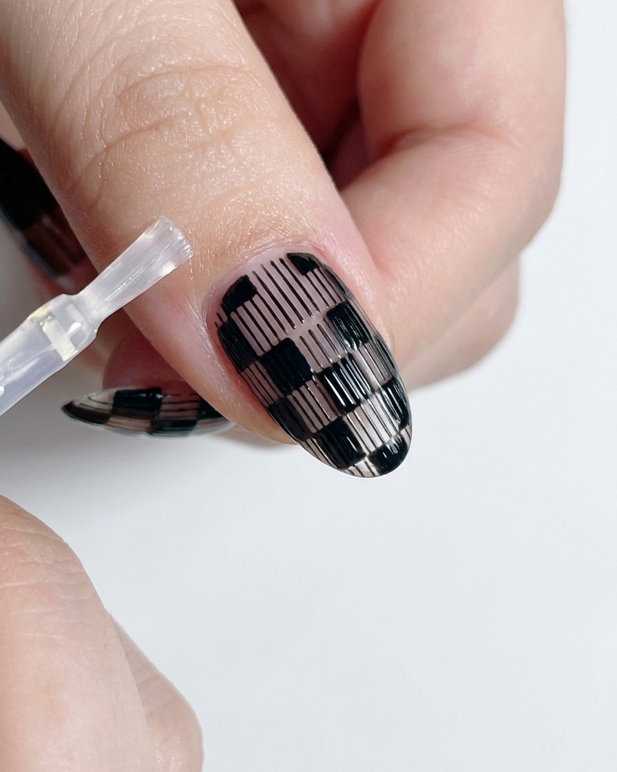 Un pennello per top coat che applica smalto trasparente lucido su ununghia finita a quadretti bianchi e neri.