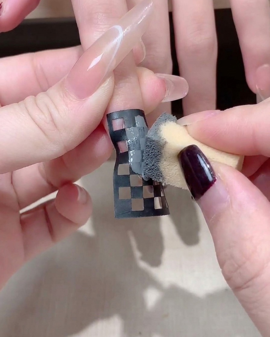 Primo piano di una manicure che regola un adesivo per unghie a scacchi bianco e nero su ununghia quadrata lunga.