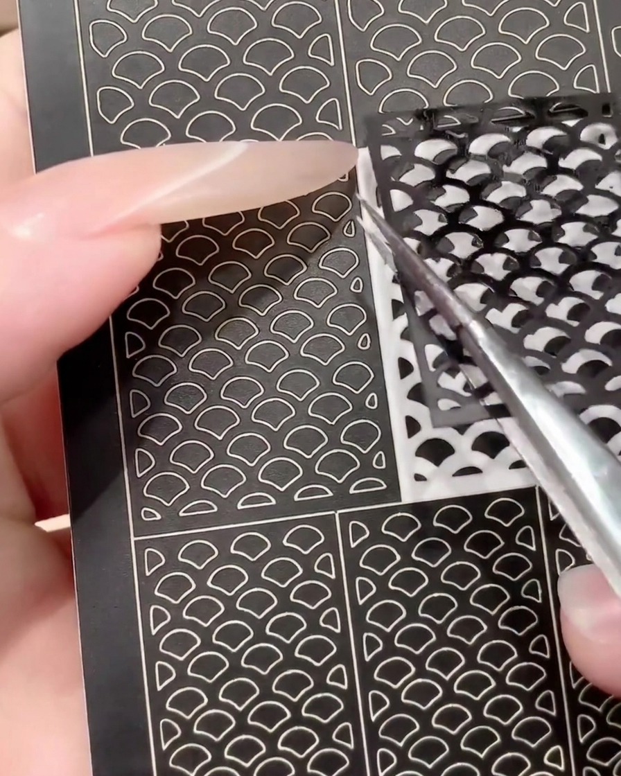 Un paio di pinzette che rimuovono un foglio di adesivi per nail art nero usato per mostrarne la riutilizzabilità.