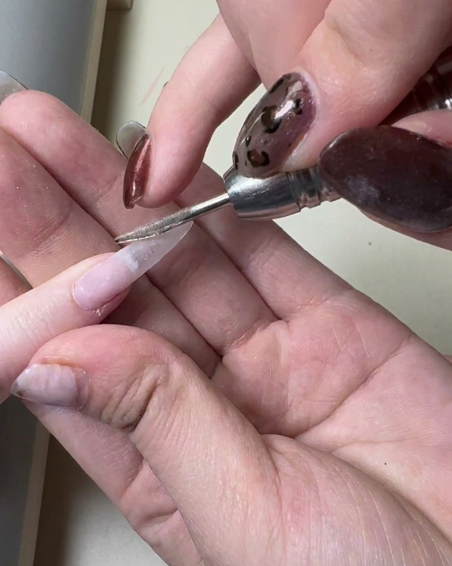 Un pennello applica un sottile strato di gel grigio traslucido su una ricostruzione unghie lunga già preparata.