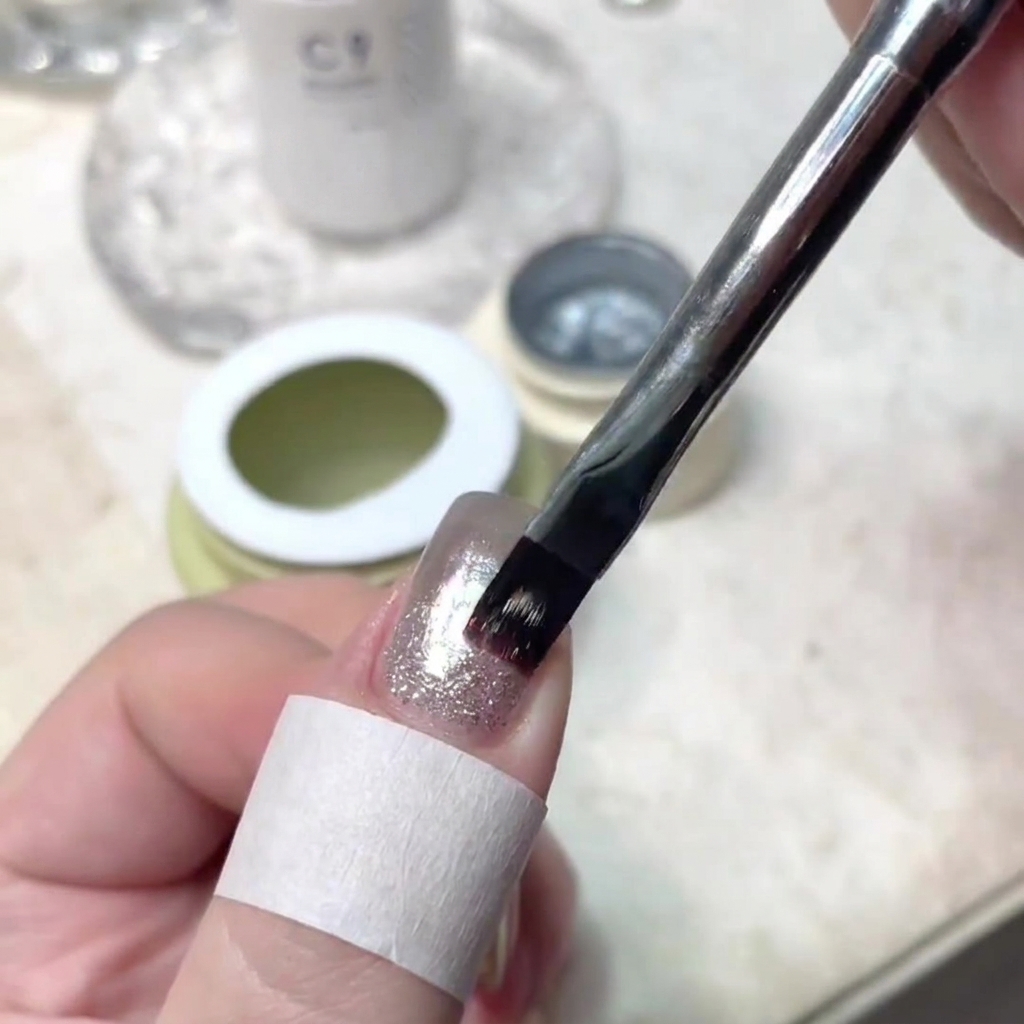 Un pennello per unghie che applica con precisione un sottile strato di gel brillante al centro di ununghia manicurata.