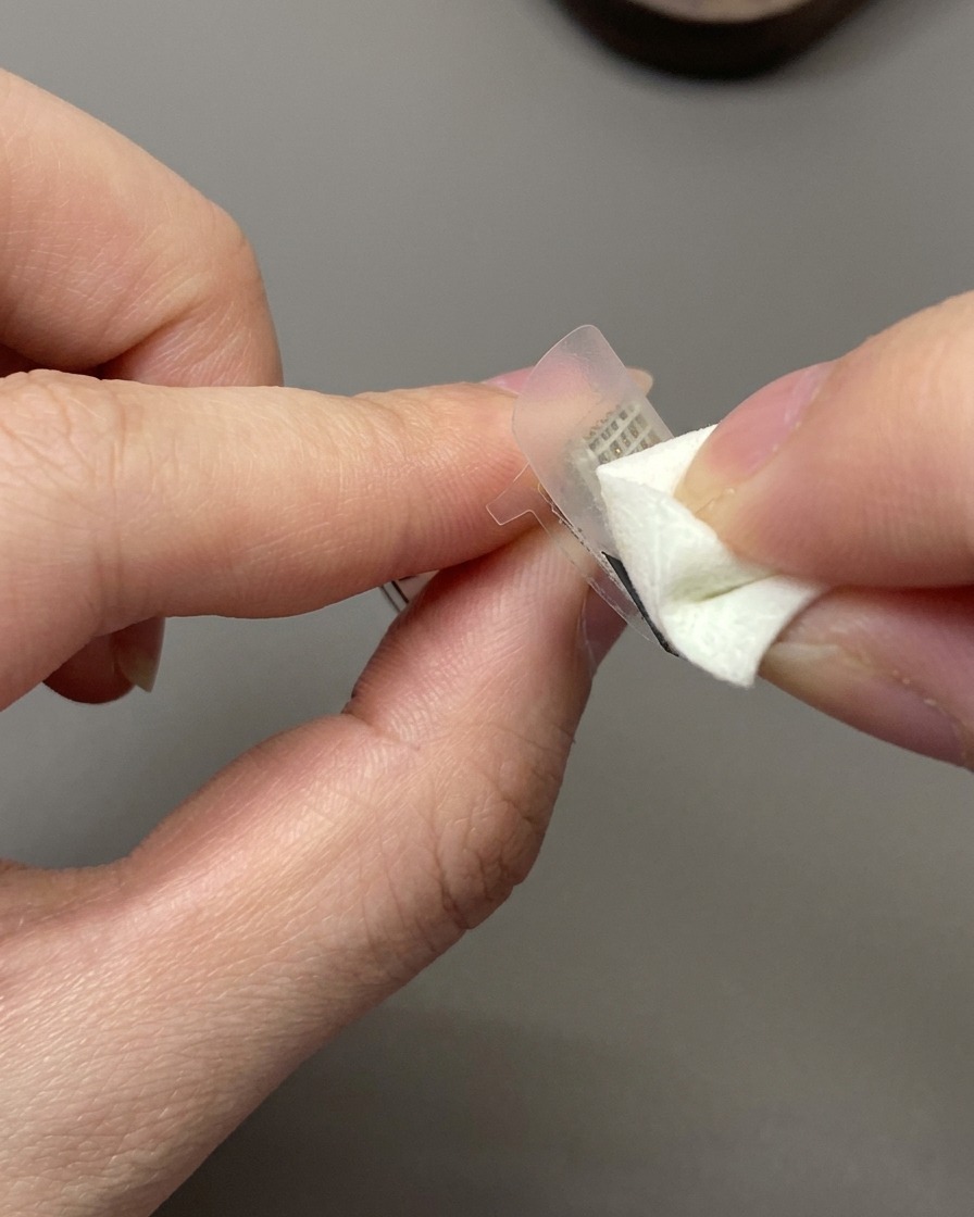 Una spugnetta cosmetica che tampona lo smalto gel bianco latte su un adesivo guida per French applicato su ununghia.