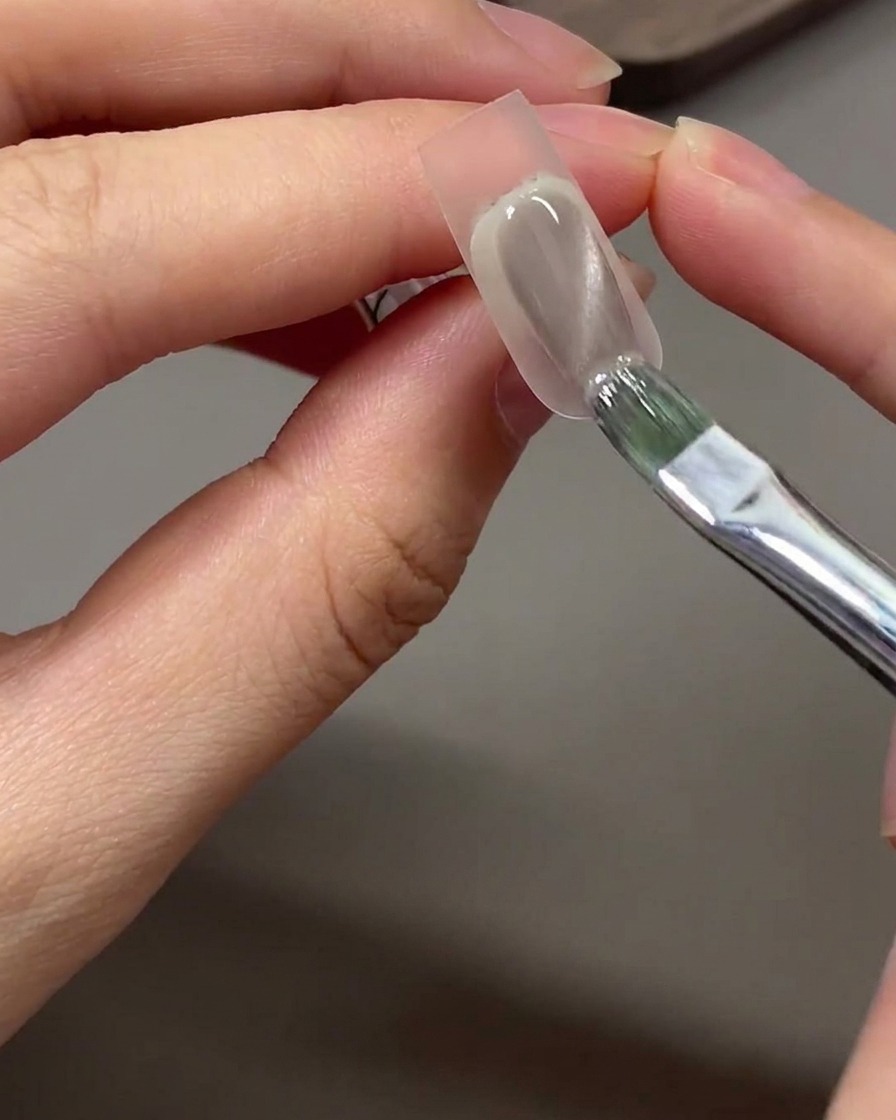 Un pennello che applica lo smalto gel cat eye grigio-nude sullarea della punta tamponata con la spugnetta.