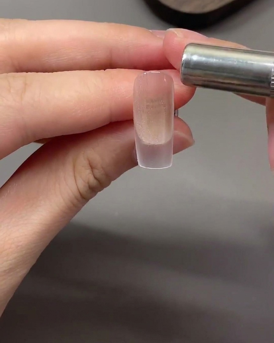 Un magnete cilindrico tenuto orizzontalmente vicino alla punta dellunghia per attirare le particelle magnetiche cat eye in una fascia di luce.