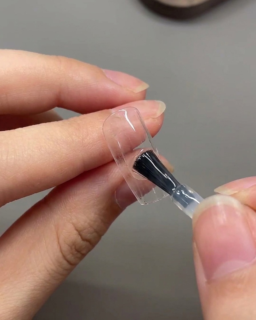 Un pennello che applica uno strato di top coat opaco su tutta la superficie dellunghia.