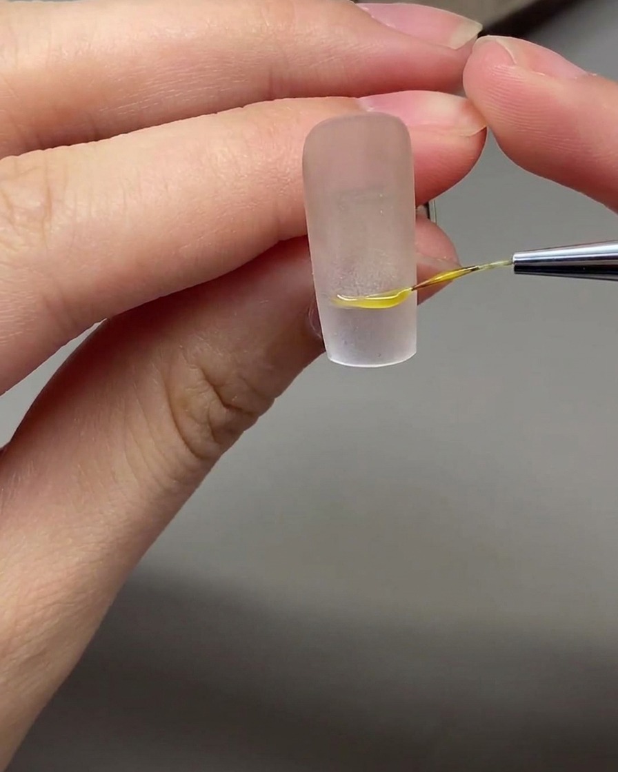 Un pennello sottile per nail art che disegna una linea del sorriso French bianca e precisa su ununghia con base nude.