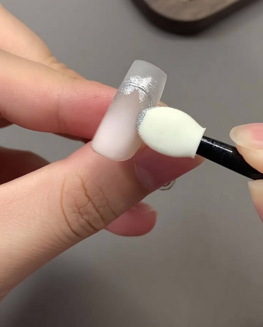 Un applicatore in spugna per ombretto che sfrega la polvere cromata argento su un disegno per unghie.