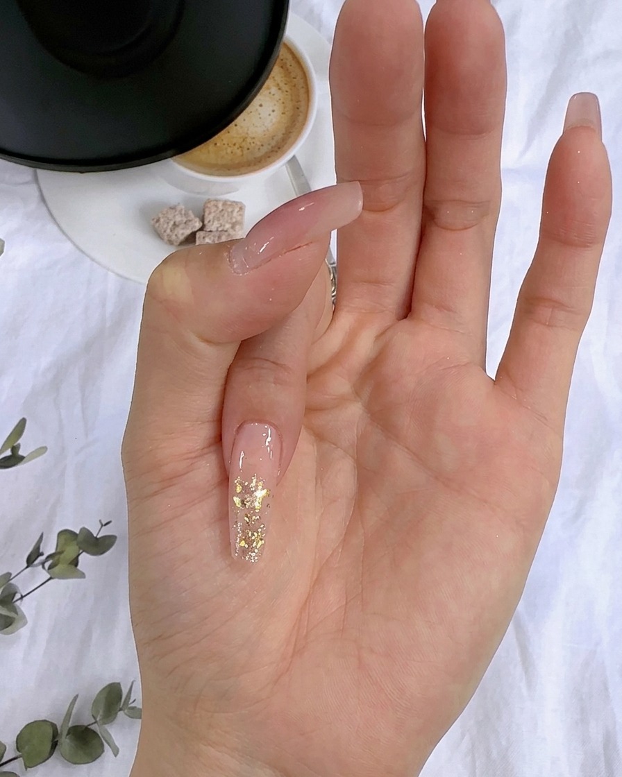 Primo piano di fiocchi di foglia doro premuti sullo strato di glitter bagnato di ununghia.