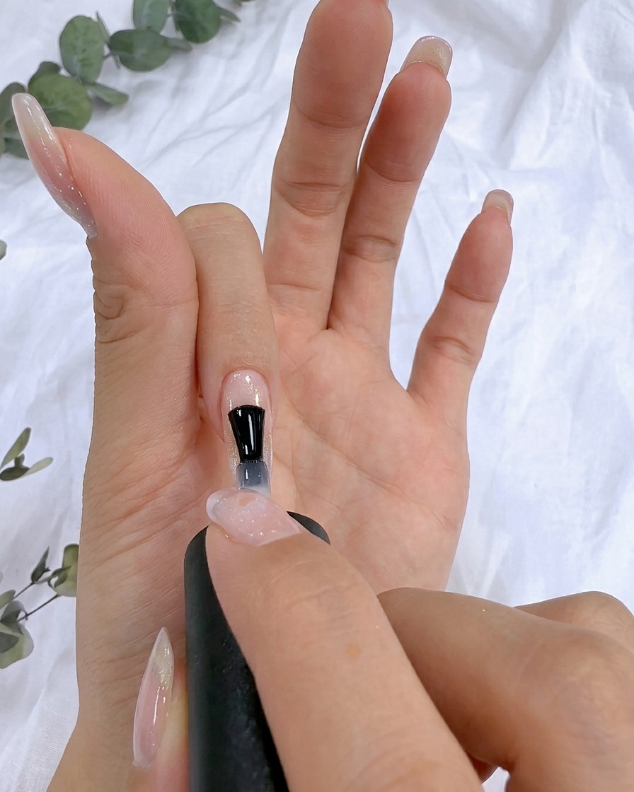 Un pennello applica del gel rinforzante trasparente sulla superficie dellunghia naturale.