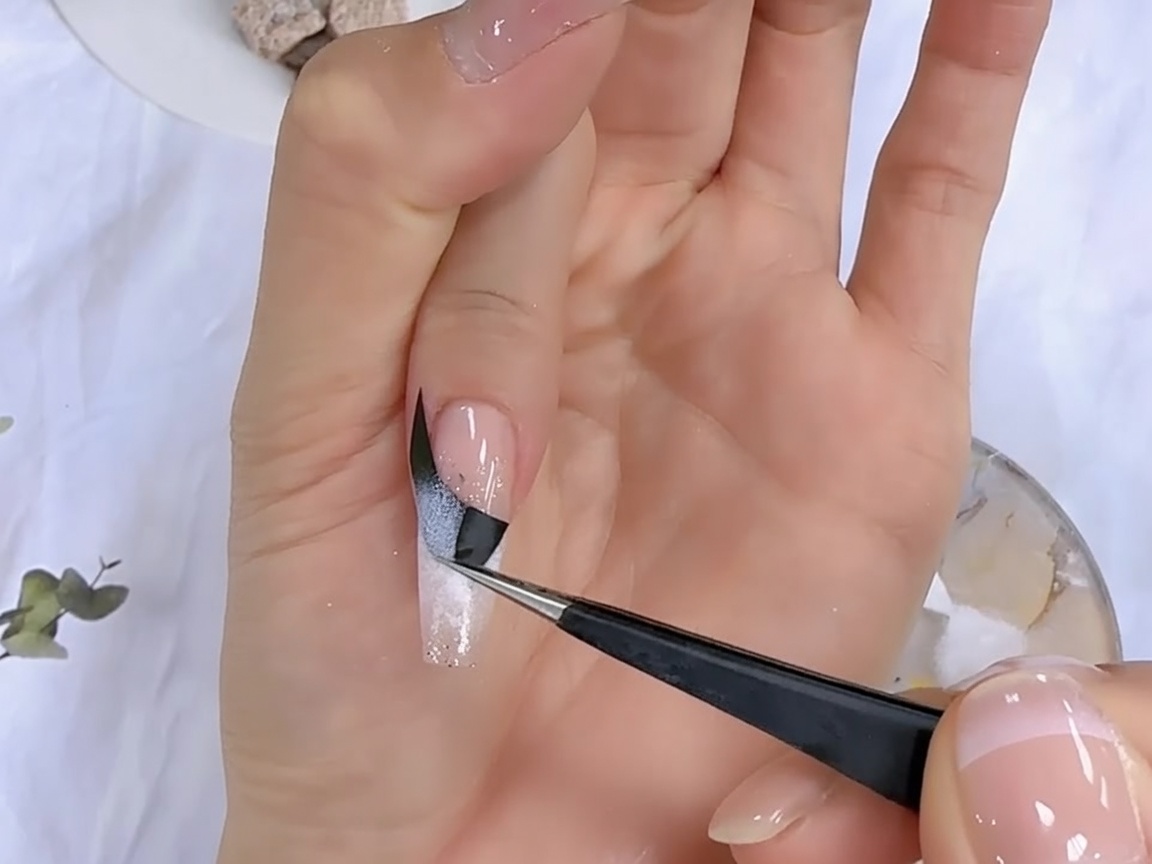 Delle pinzette rimuovono un adesivo nero per french da ununghia per rivelare il design sfumato sottostante.