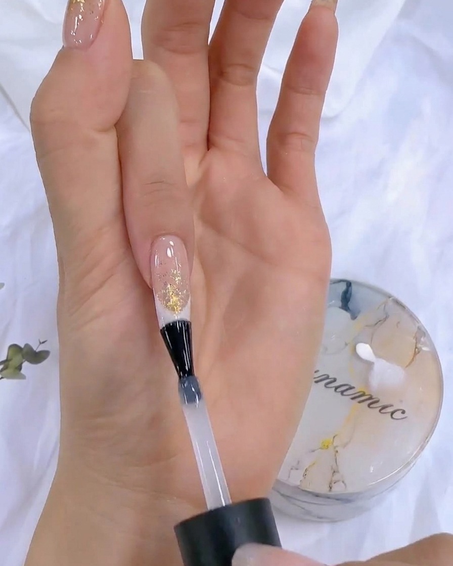Una mano con un flacone di top coat vicino a una lampada UV/LED durante la fase finale di polimerizzazione.