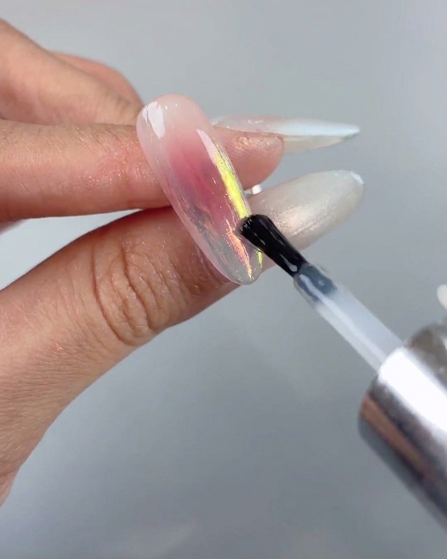 Un pennello per unghie che applica uno strato finale sigillante di top coat liscio sopra un design con unghie cromo aurora.