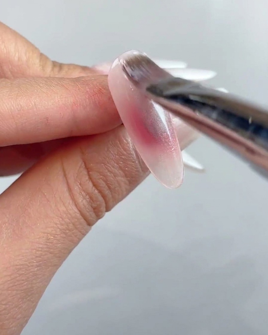 Un pennello per unghie che applica uno strato di gel cat-eye trasparente su tutta la superficie dellunghia preparata.