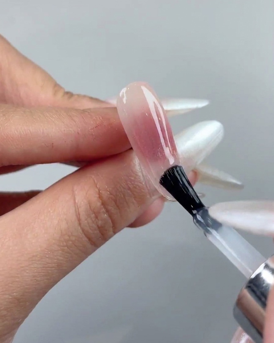 Un pennello che applica uno strato di top coat trasparente su ununghia in gel cat-eye polimerizzata.