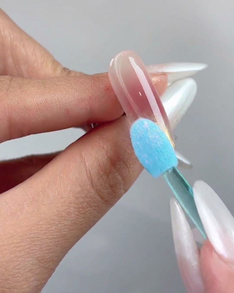 Un applicatore in spugna di silicone blu che pressa la polvere cromo aurora sulla punta di ununghia.