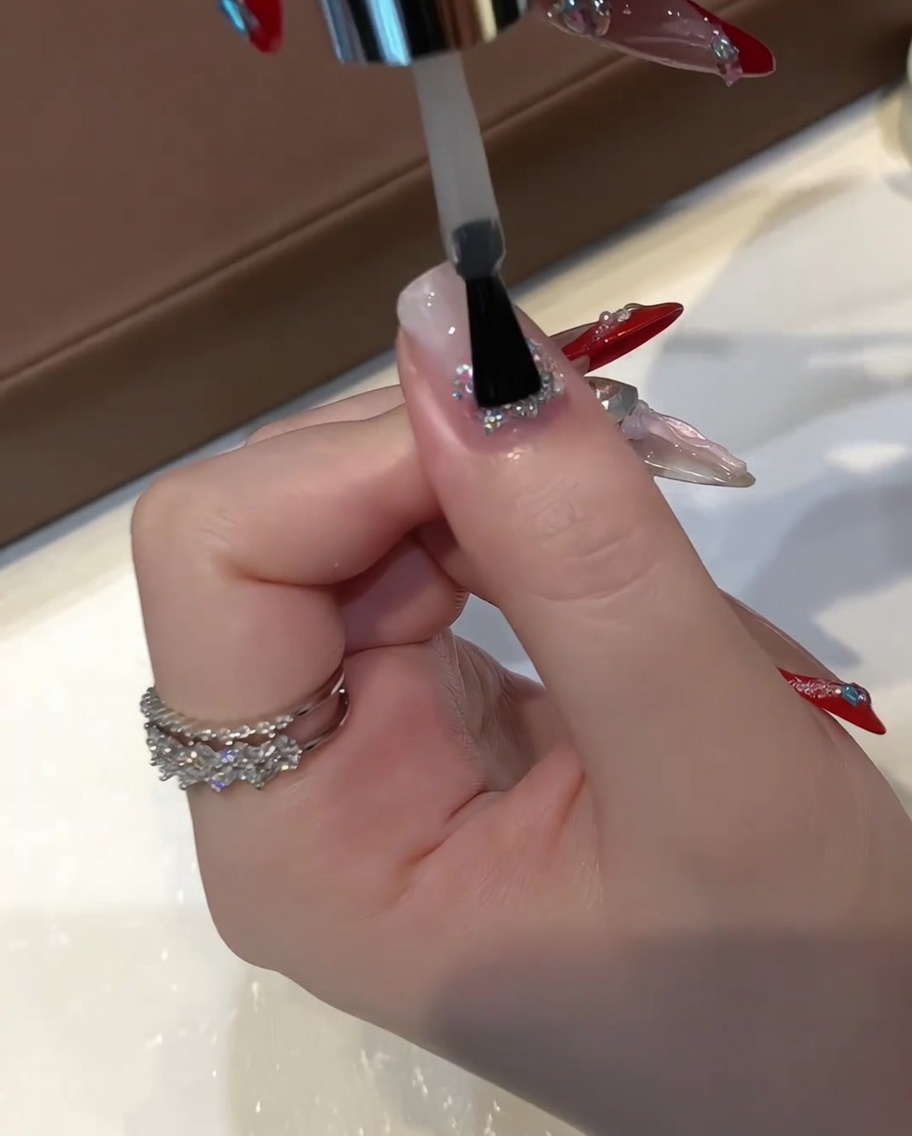 Un pennello piatto per gel applica uno strato spesso di gel costruttore autolivellante trasparente su ununghia con glitter incapsulati.