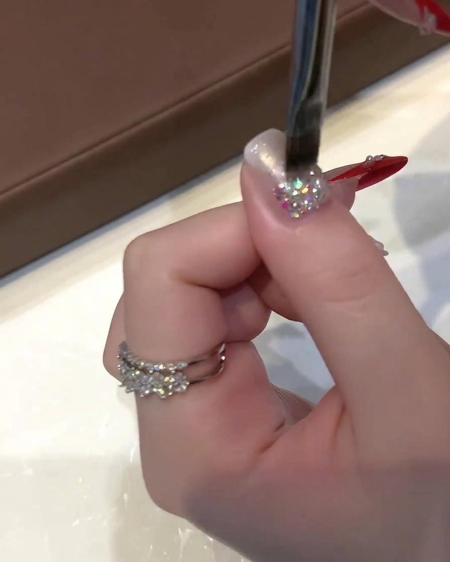 Una mano che regge un pennello piatto per gel applica uno smalto cat-eye dorato-argentato semitrasparente su ununghia glitterata.