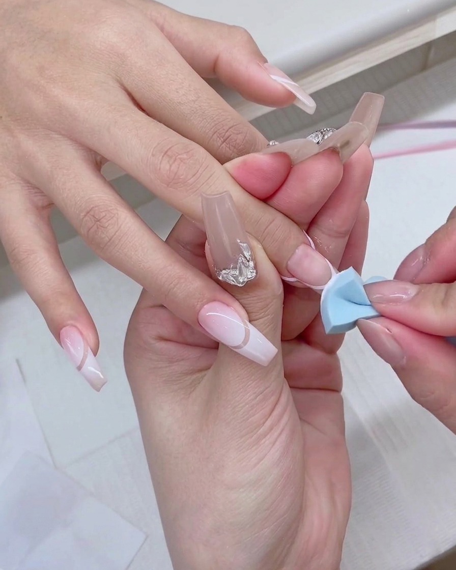 Una spugnetta blu da trucco viene delicatamente picchiettata sulla punta di ununghia per creare un effetto sfumato bianco.