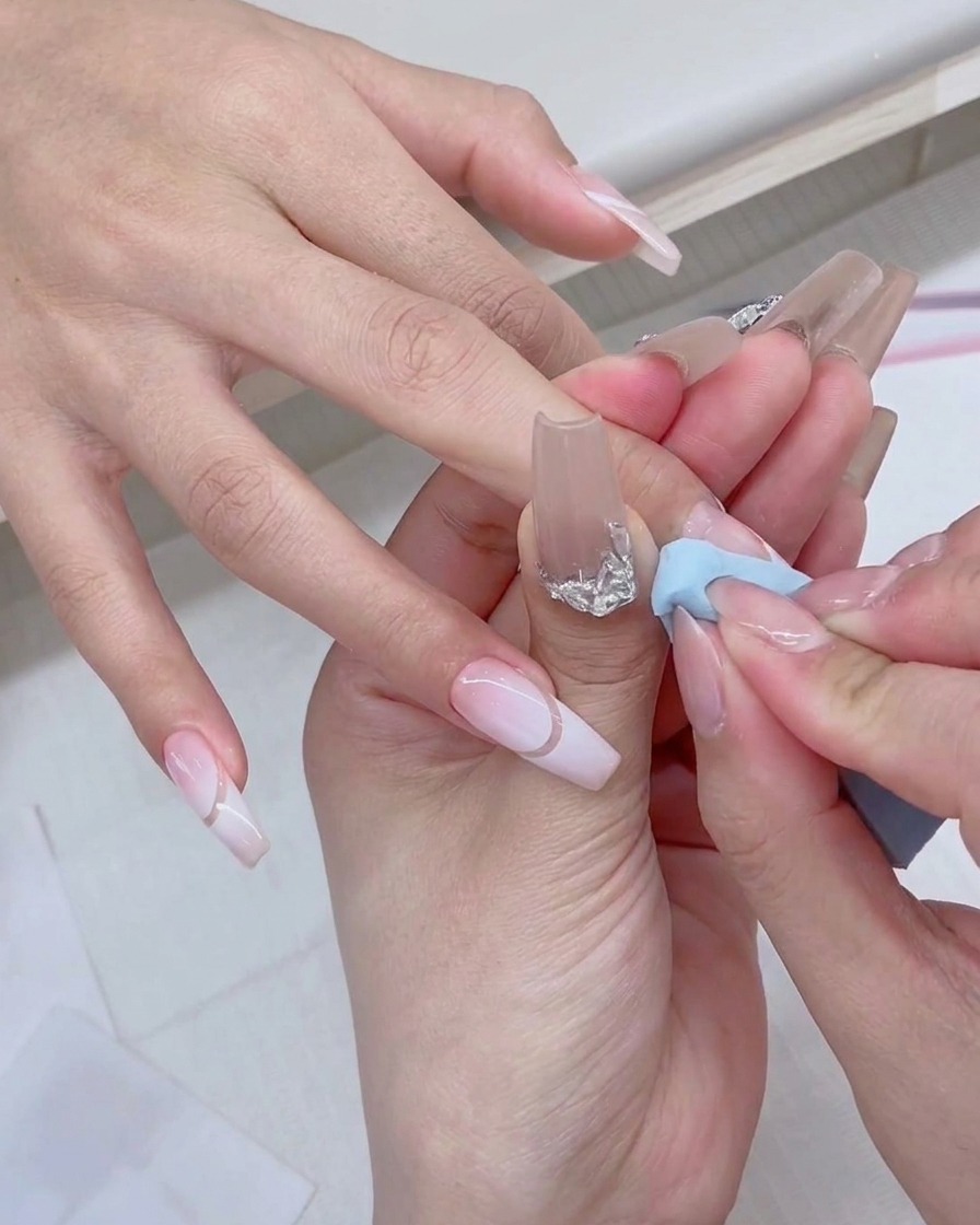 Un pennellino per smalto gel dipinge del prodotto bianco fresco direttamente sul bordo di una spugnetta da trucco blu.