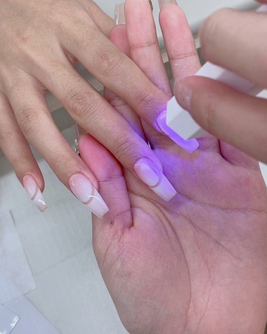 Una mano riposa allinterno di una lampada per unghie UV/LED rosa con luce viola che illumina le unghie preparate.