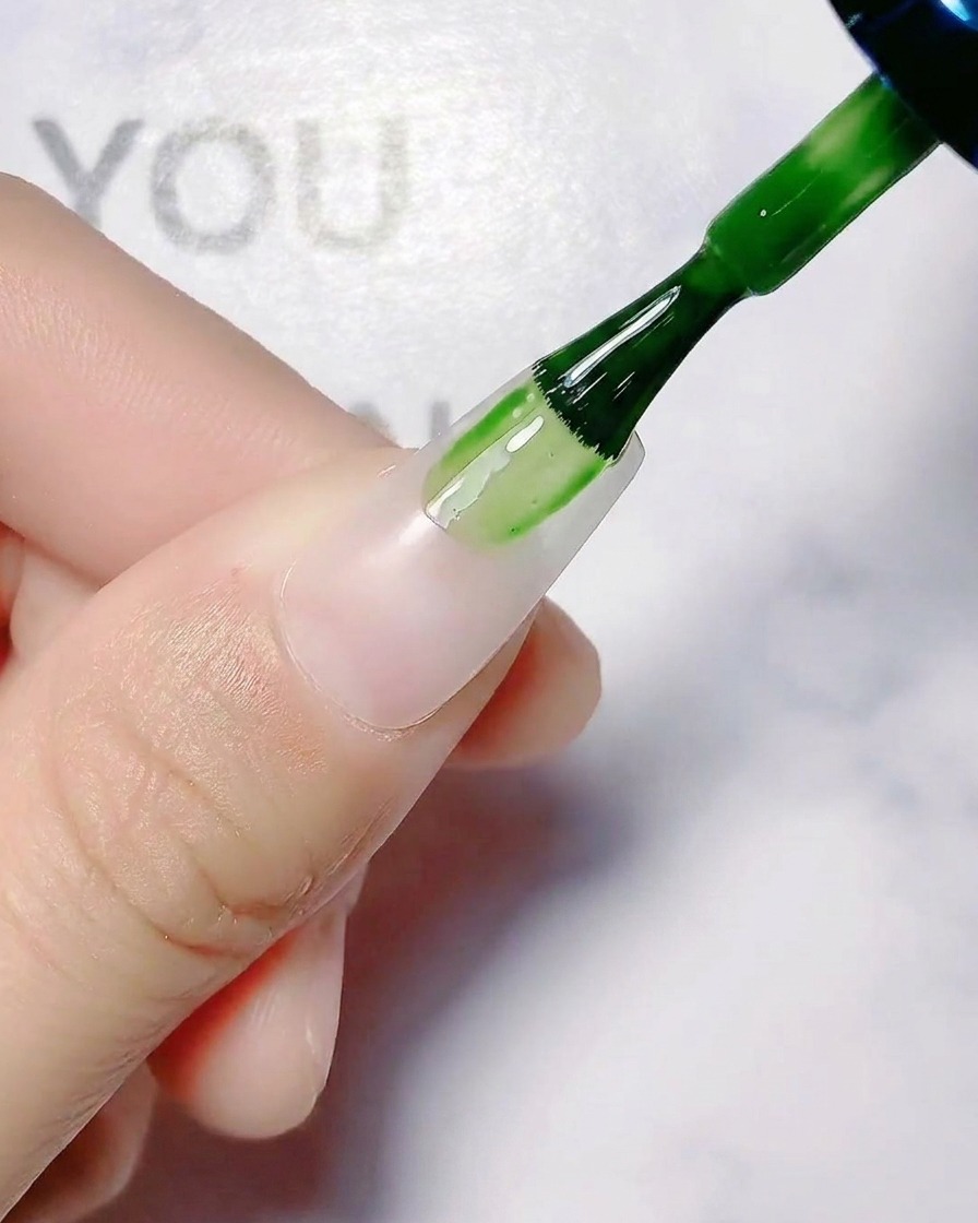 Un pennello per unghie applica una base coat bianca traslucida su ununghia naturale.