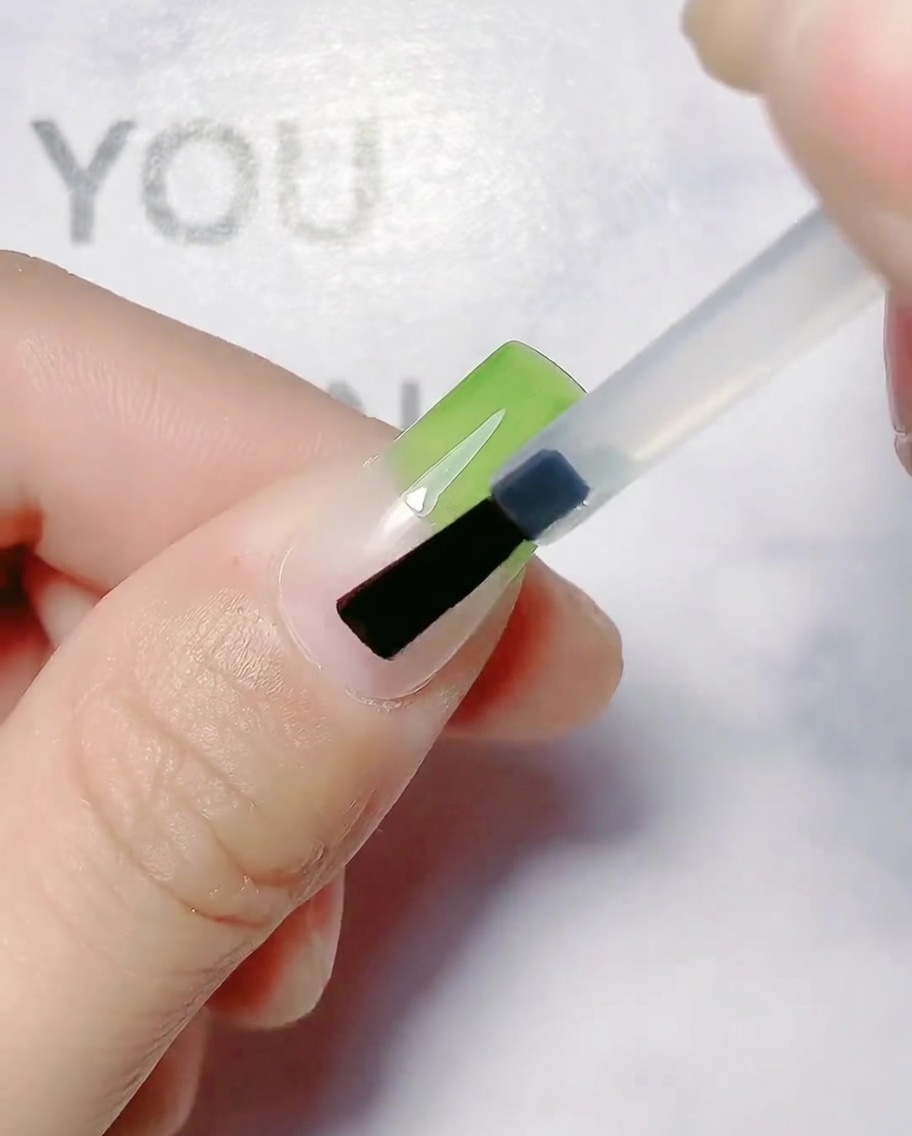 Un pennello applica il gel verde oliva sulla metà superiore di ununghia naturale.