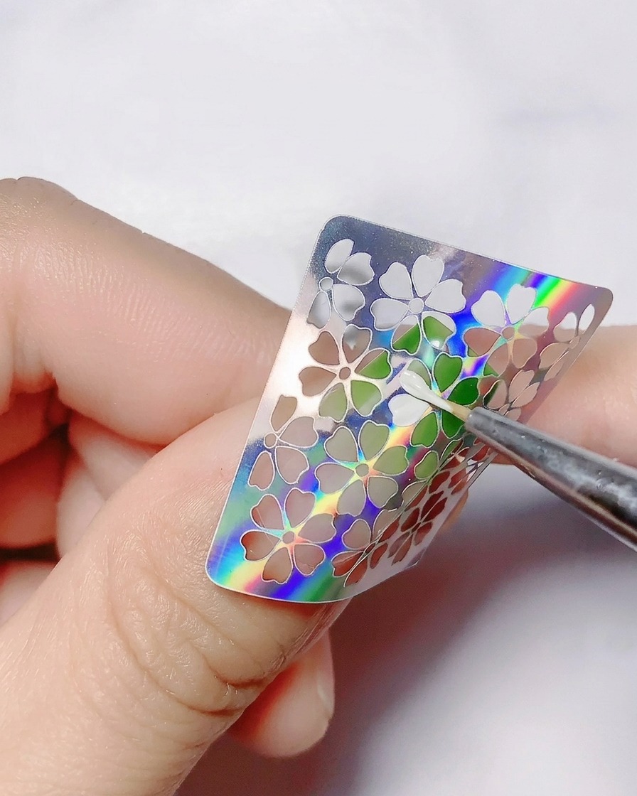 Un pennello fine applica il gel colorato bianco allinterno dei ritagli floreali vuoti di un adesivo.
